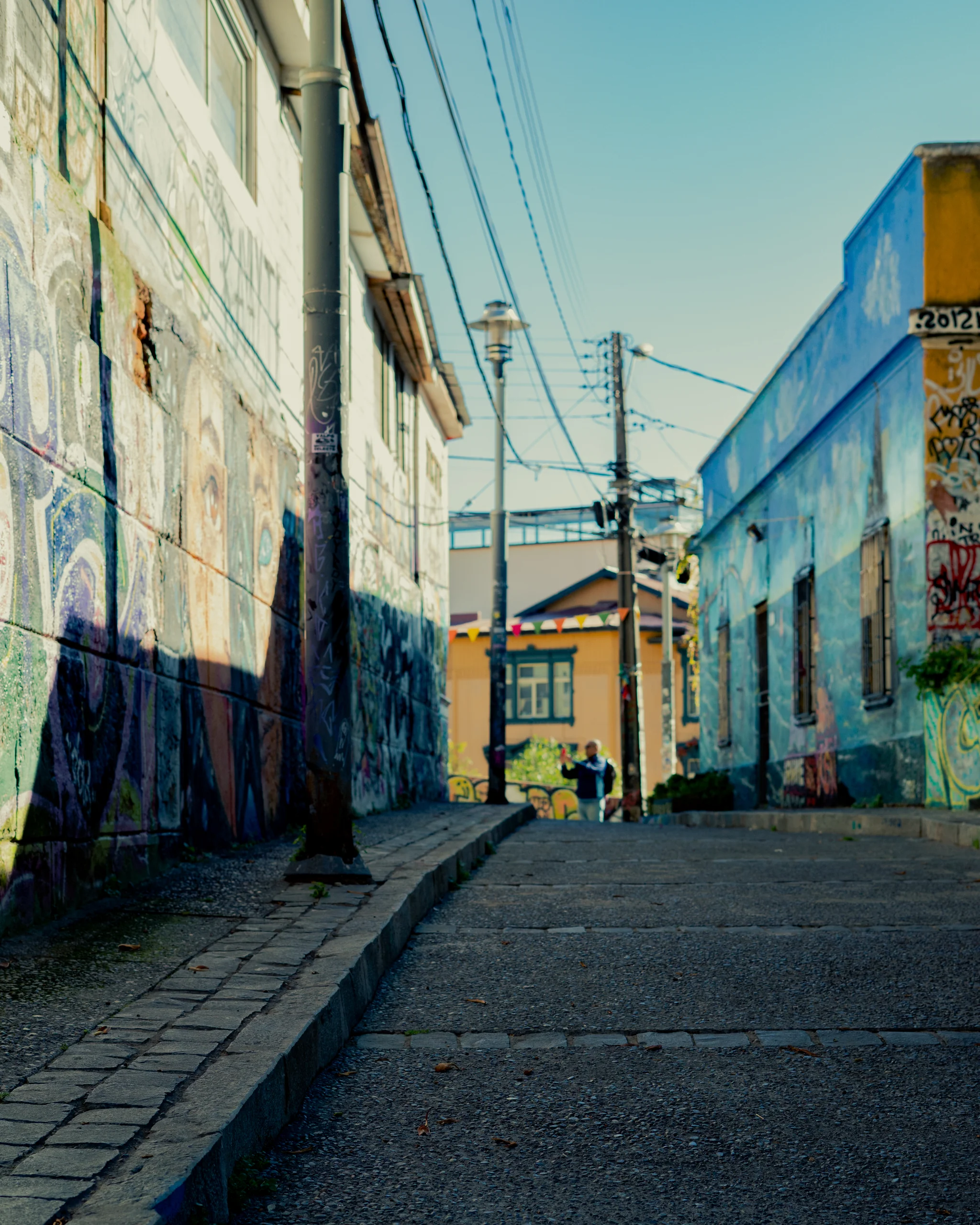 Callejón en pendiente, muros pintados y alguien al fondo que simplemente vive su día mientras yo cuadro la toma.