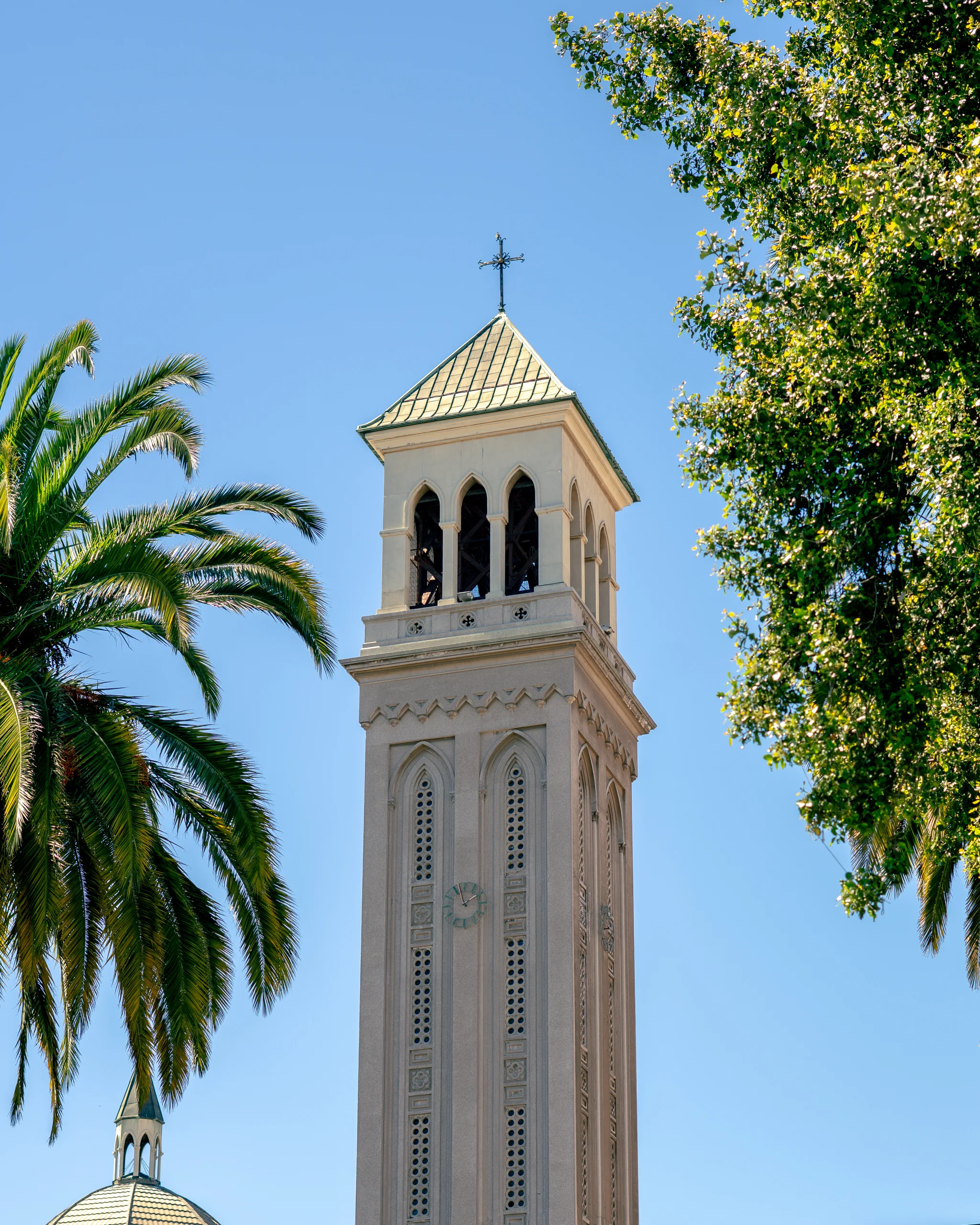 Una torre de iglesia recortada en el cielo, rodeada de árboles y un día despejado.