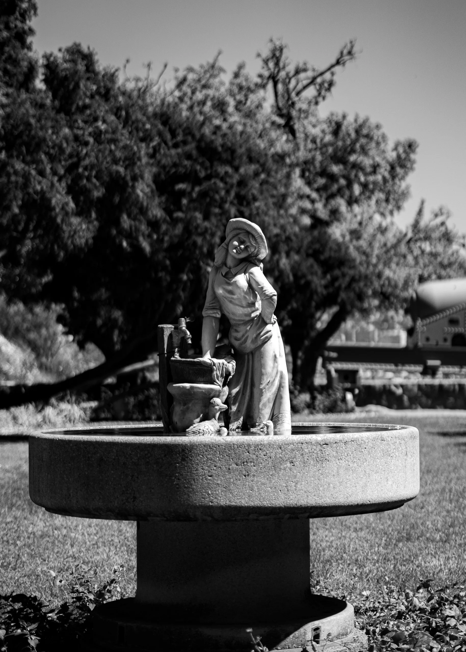 Figura femenina junto a una fuente, rodeada de verde, como si el tiempo se hubiera frenado ahí.