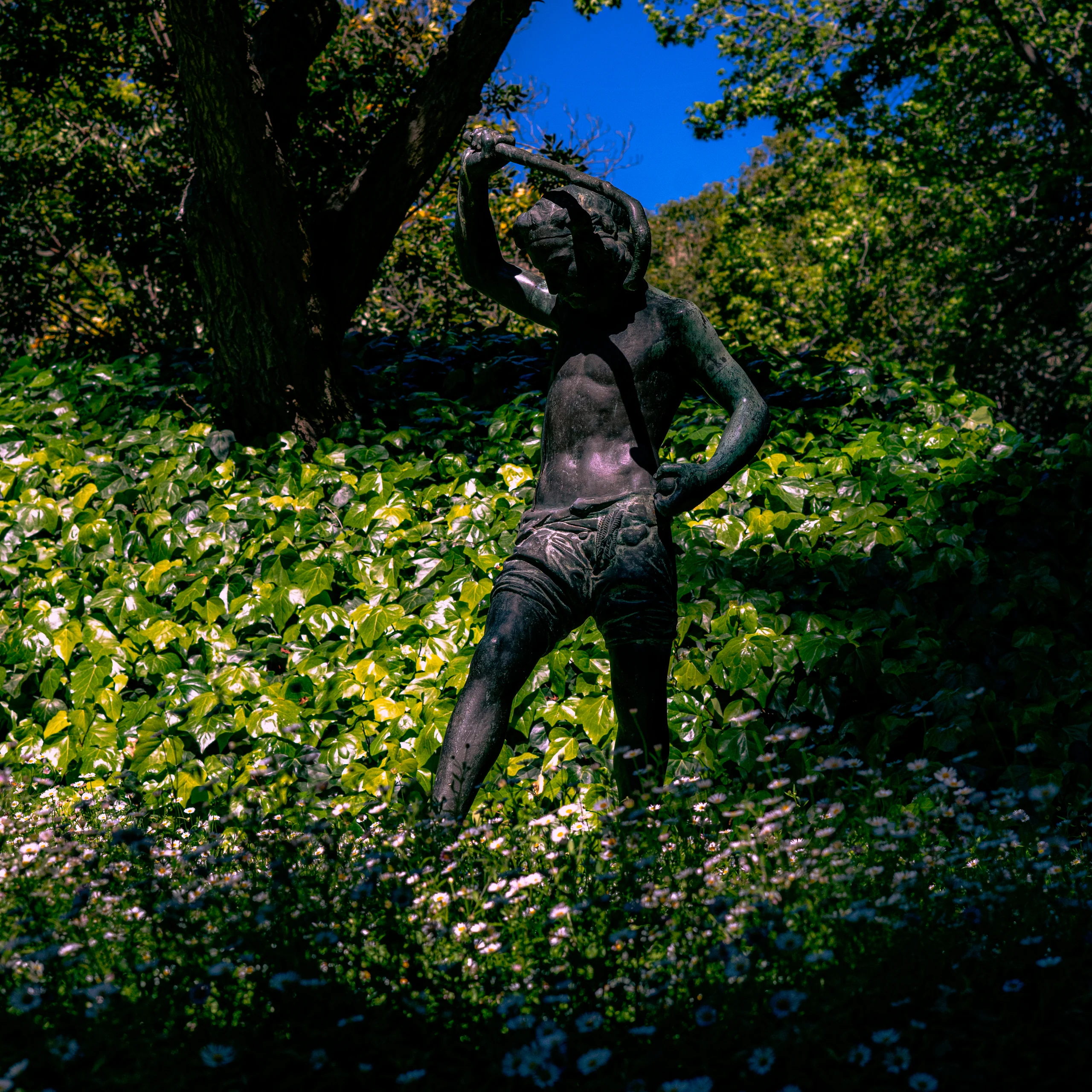 Escultura de un niño en medio del jardín, concentrado en su propio juego silencioso.