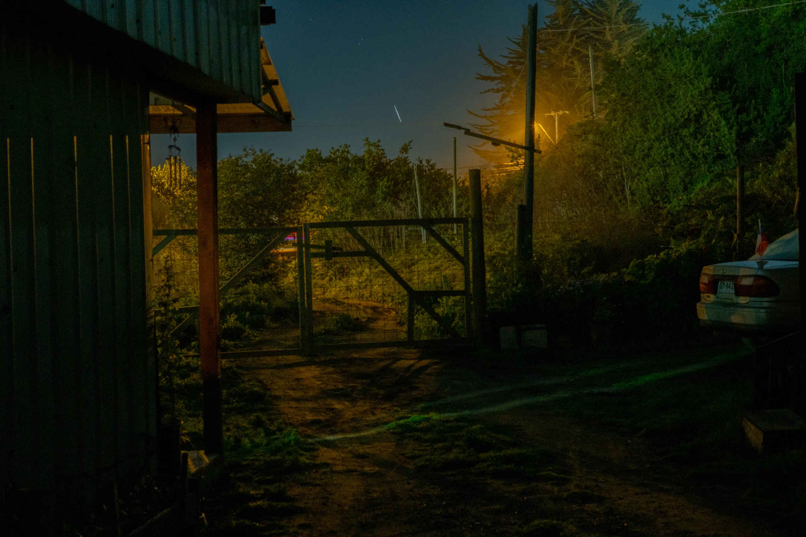Camino rural iluminado por luz artificial, mientras el cielo se pierde en oscuro profundo.